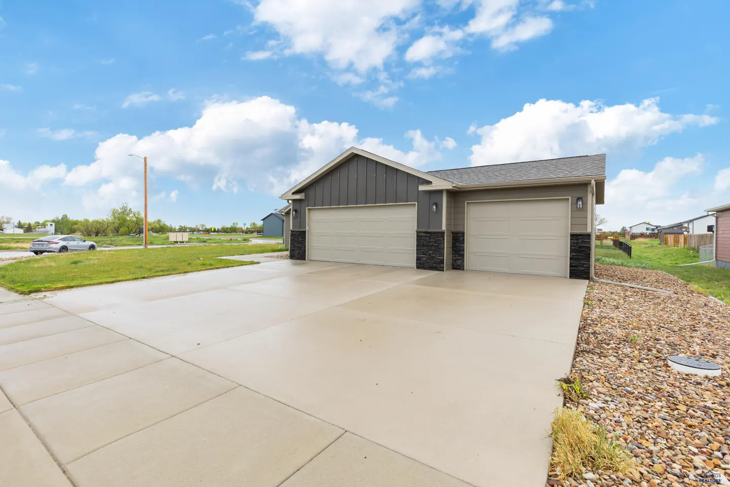 Exterior view of a modern home with a three-car garage, concrete driveway, and stone accents under a blue sky.