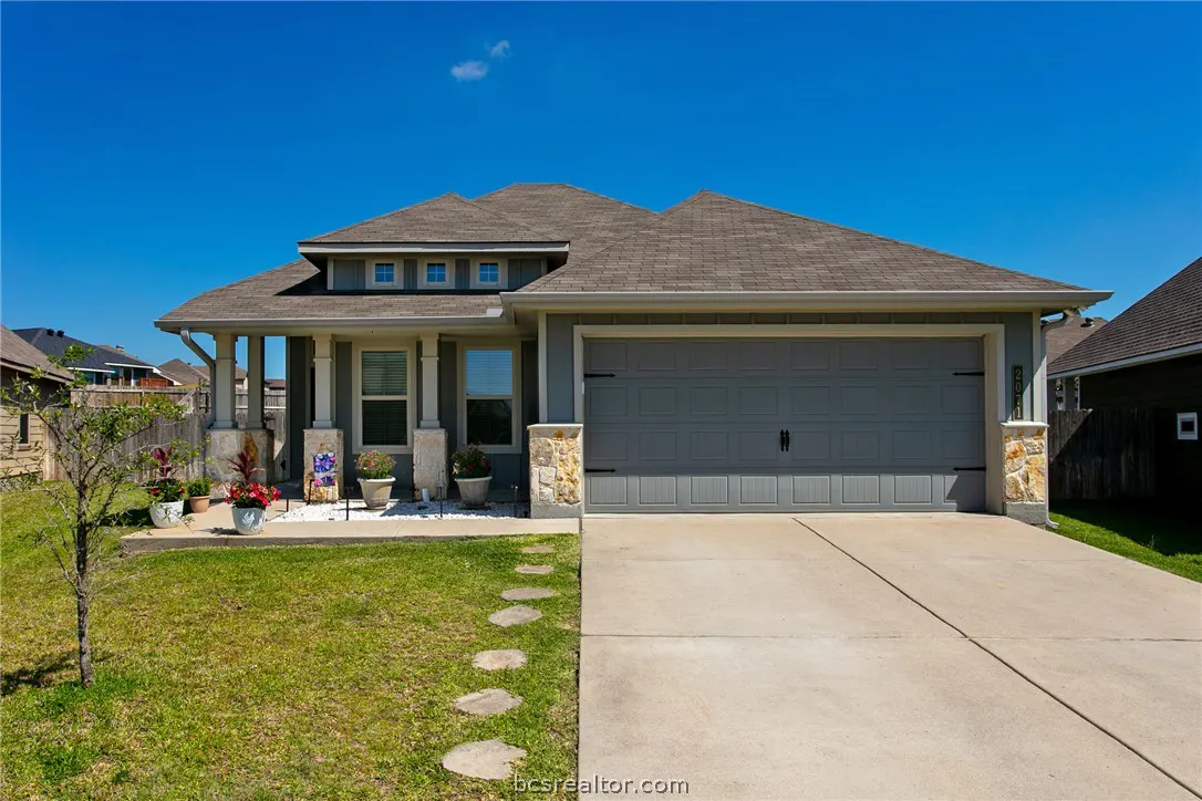 A gray single-story house with a brown roof, a two-car garage, and a green lawn under a blue sky.