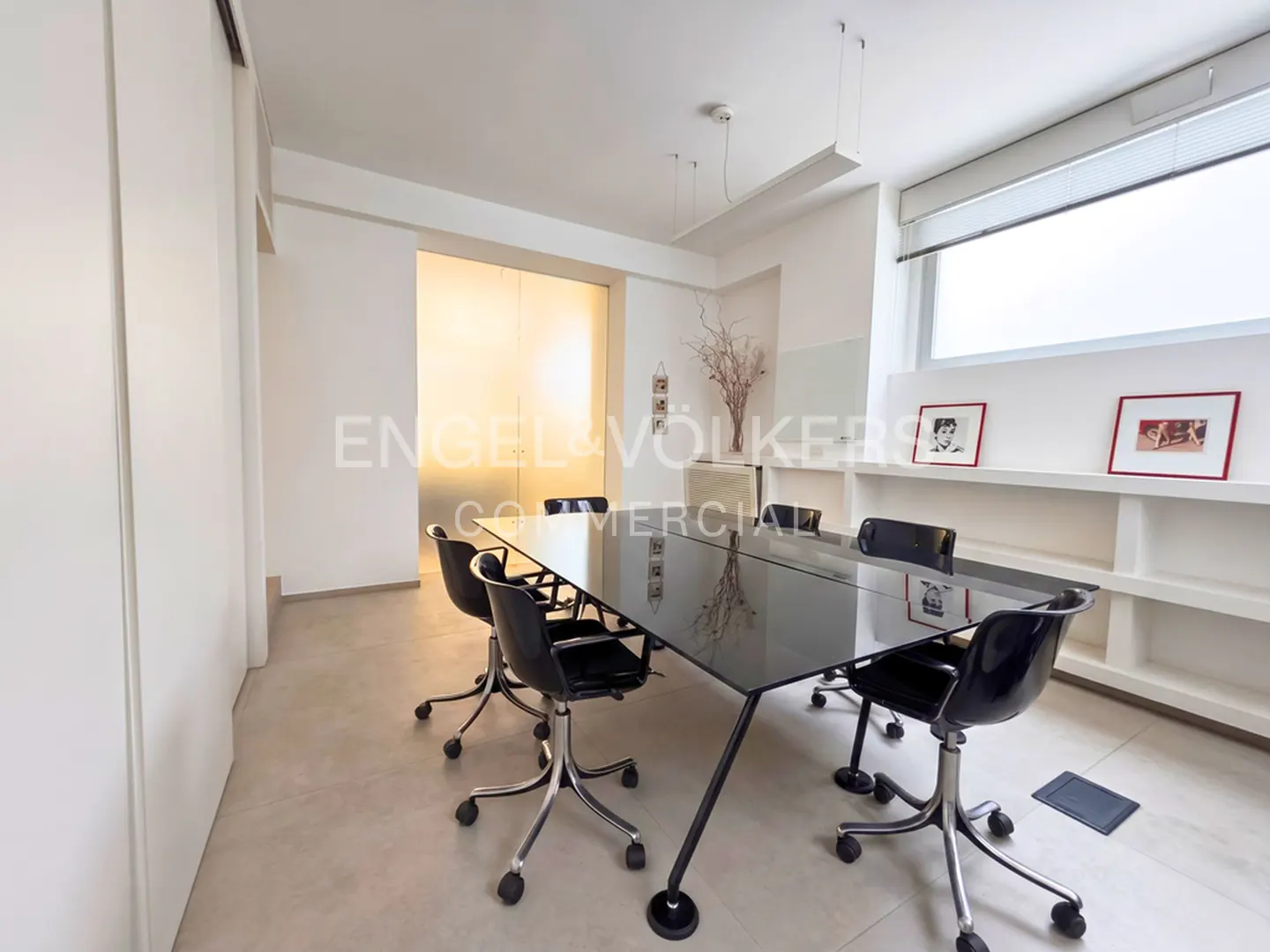 Bright office space with a black conference table, rolling chairs, and white walls with built-in shelves.