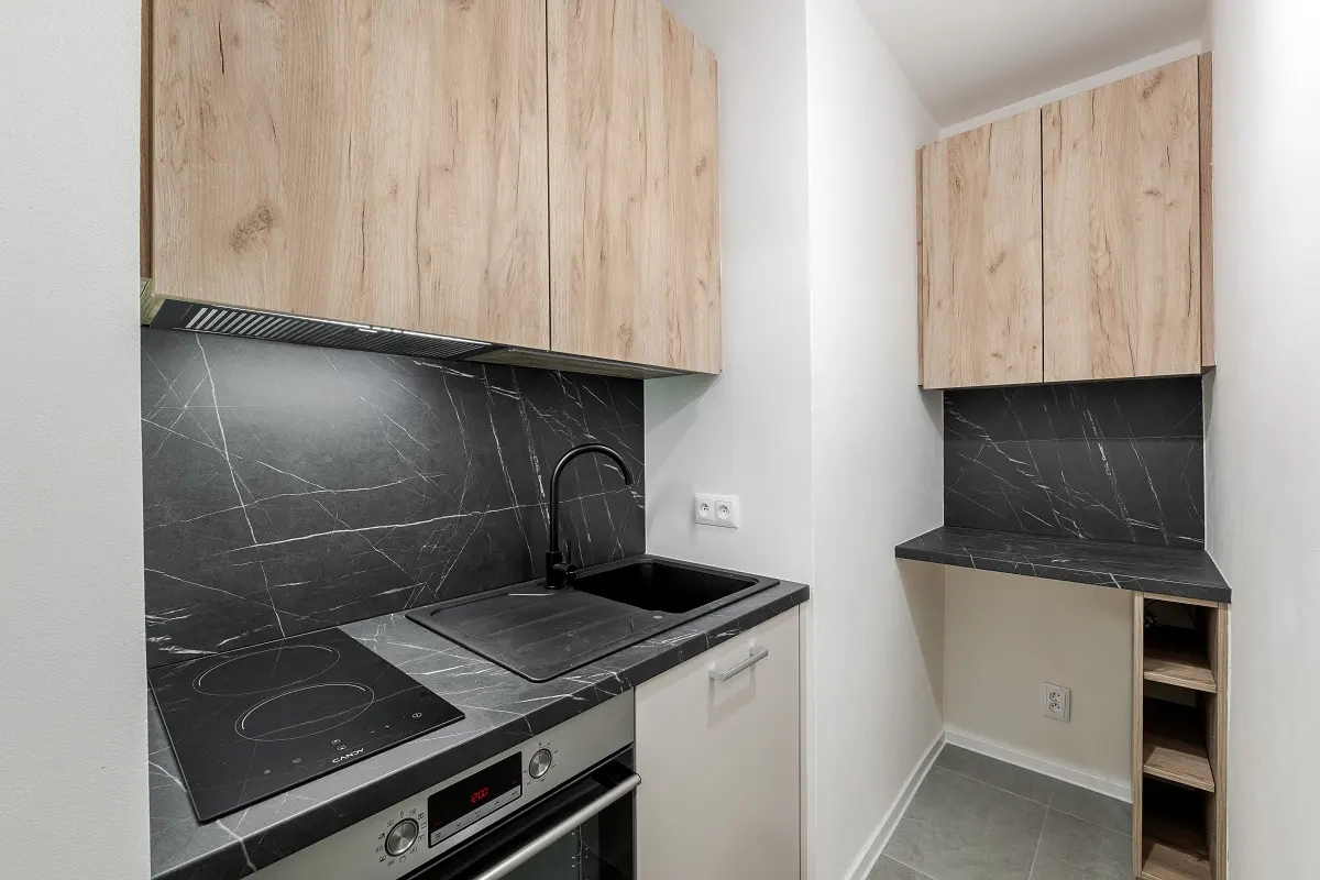 A modern kitchen with light wood cabinets, black marble backsplash, and stainless steel oven.