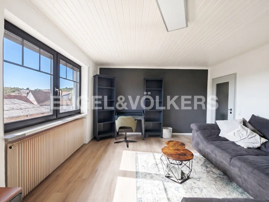 Bright living room with wood floors, black accent wall, desk, shelves, gray sofa, and a window with a view.