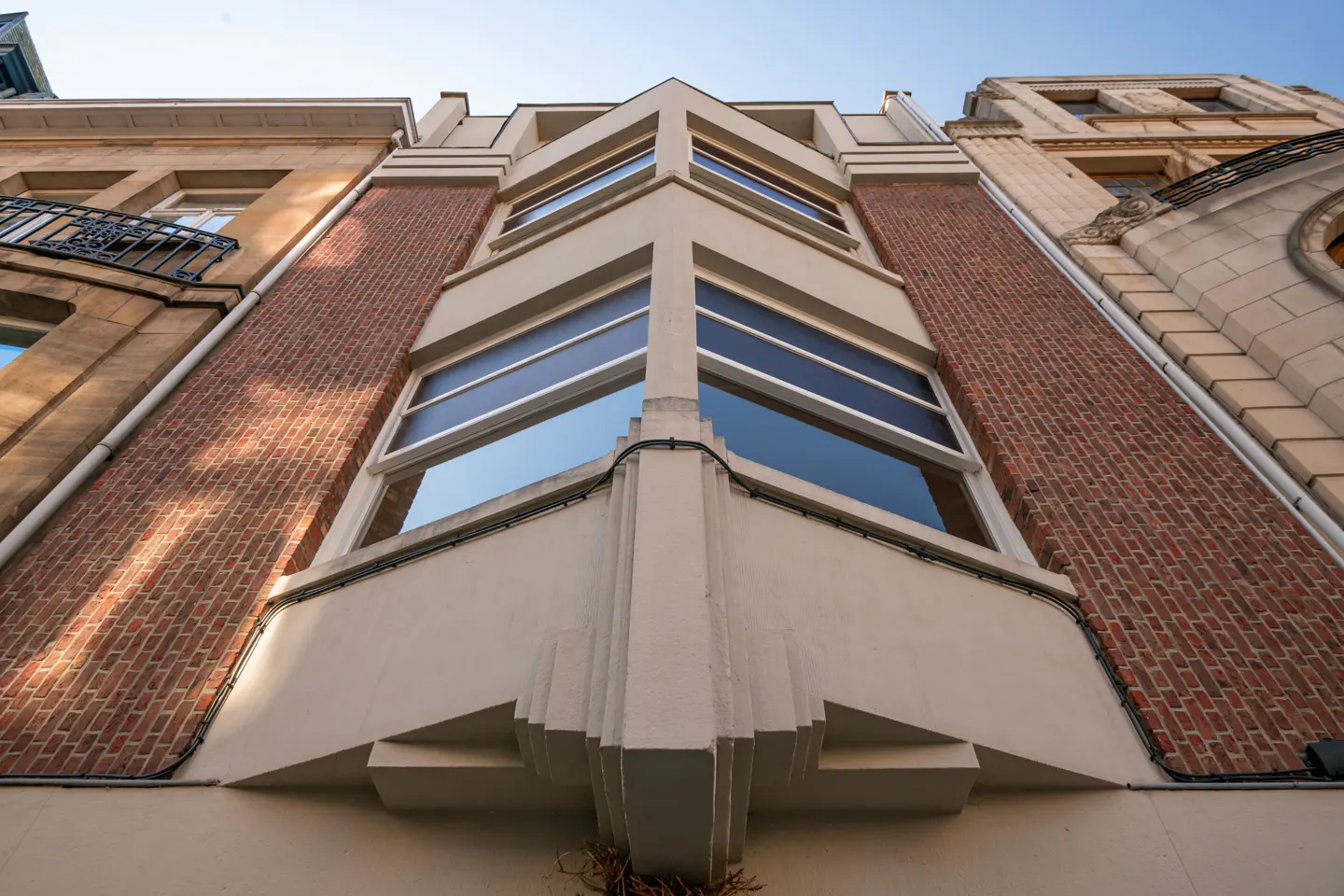 Low angle view of a building with red brick and white stone facade, featuring large windows reflecting the sky.