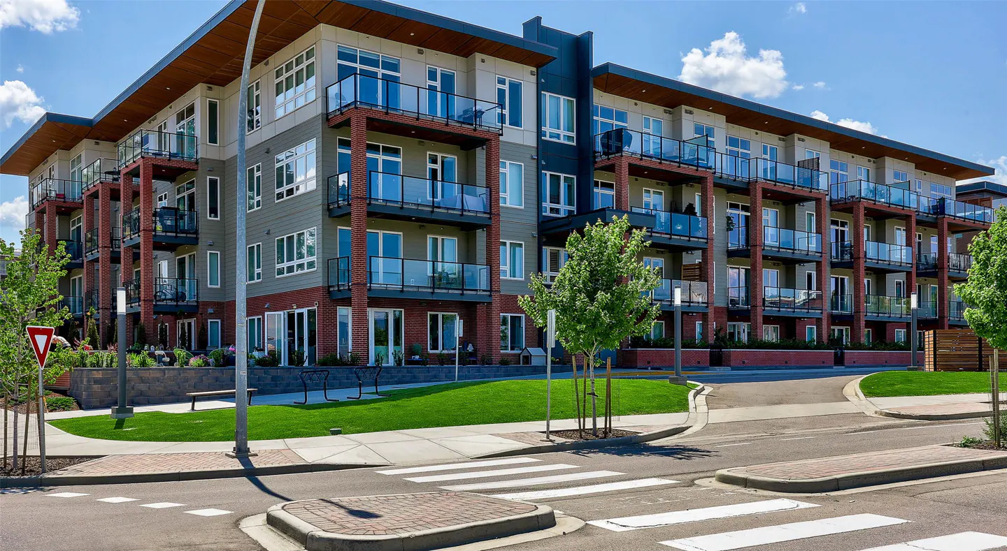 Modern apartment building with balconies, gray and brick facade, and green lawn on a sunny day.