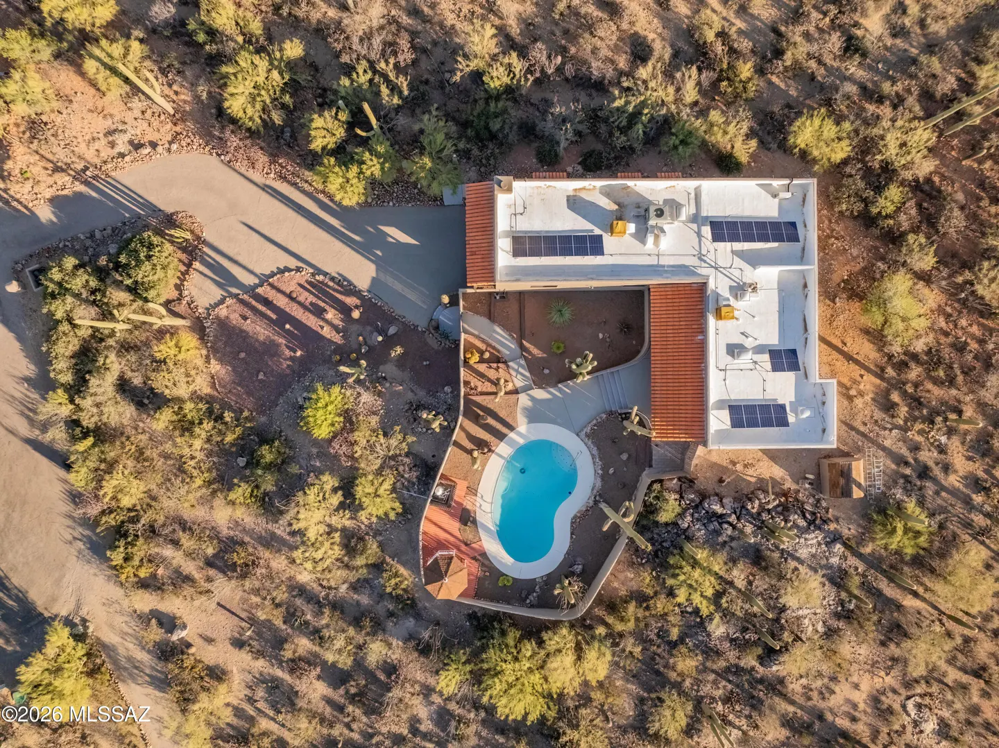 Aerial view of a modern white house with a blue kidney-shaped pool, solar panels, and desert landscaping.