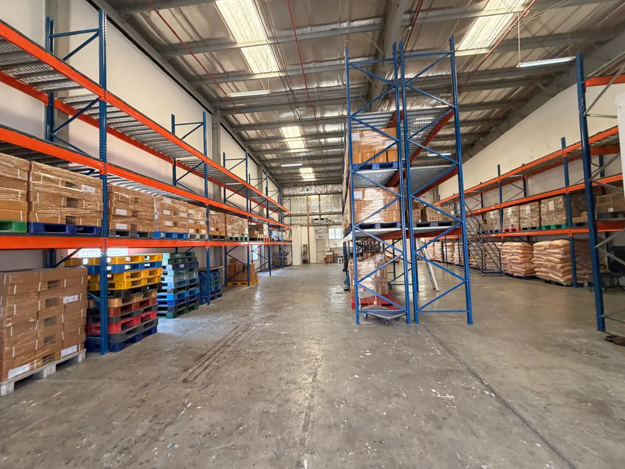 A warehouse interior with blue and orange metal shelving units filled with boxes and pallets.