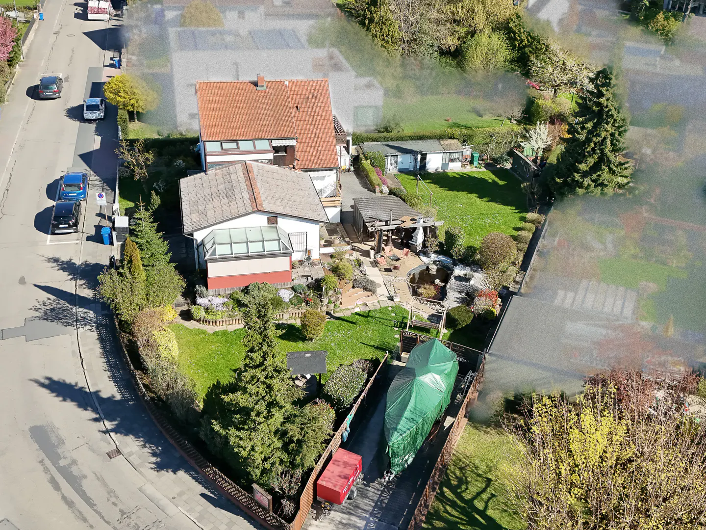 Aerial view of a house with a red tile roof, a lush green lawn, and a pond. A boat covered with a green tarp sits in the driveway.