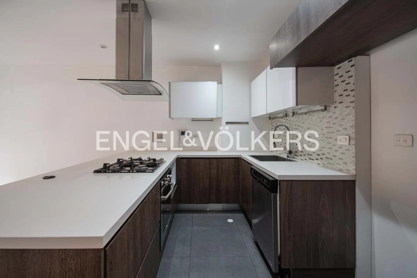 A modern kitchen with white countertops, dark wood cabinets, and stainless steel appliances.
