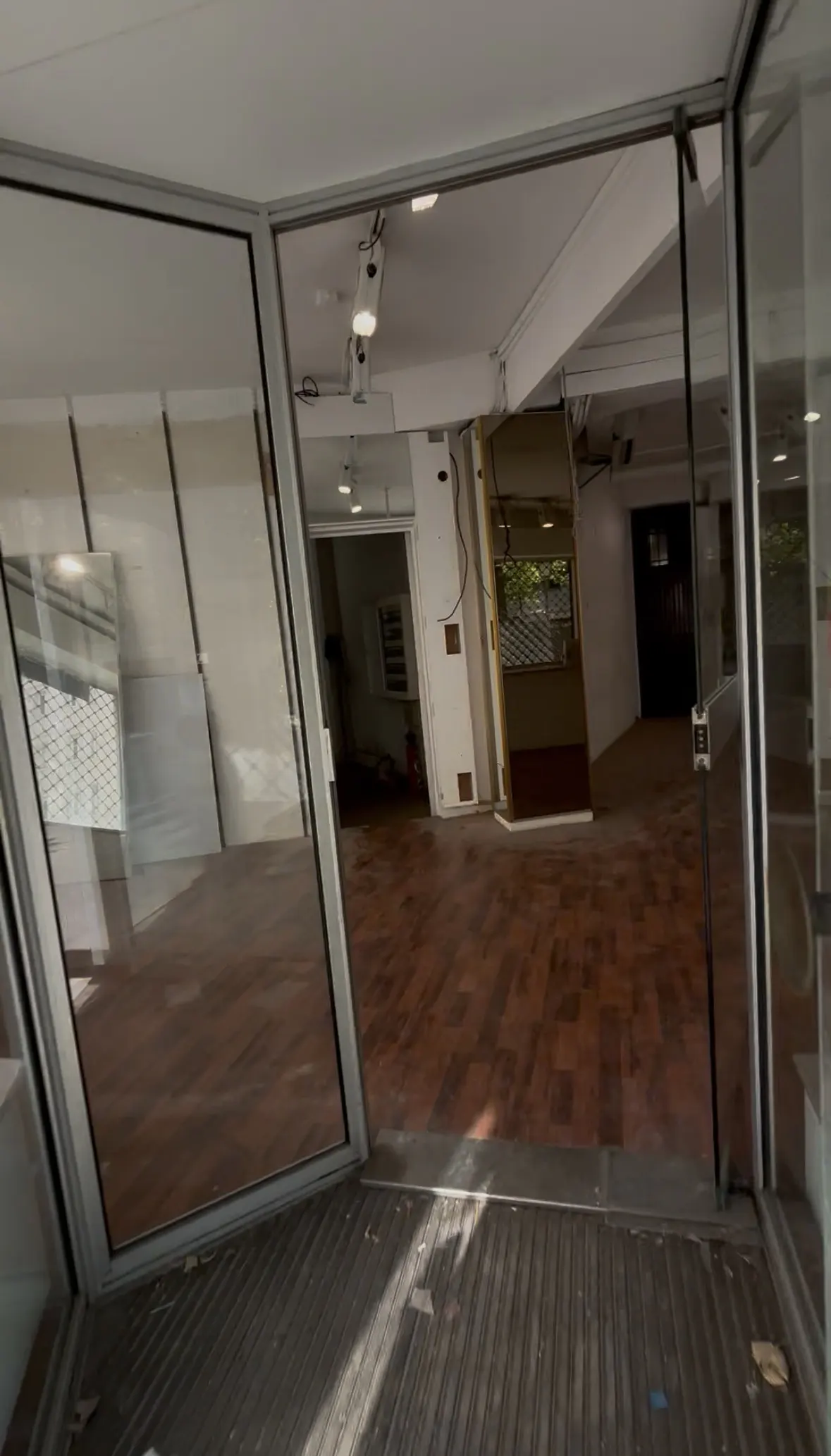 Empty retail space with glass storefront and wood floors. Interior is white with track lighting.