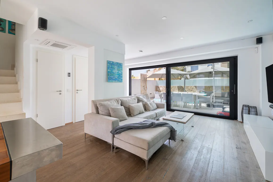 Bright living room with a beige sofa, glass table, and sliding glass doors to an outdoor patio with dining.
