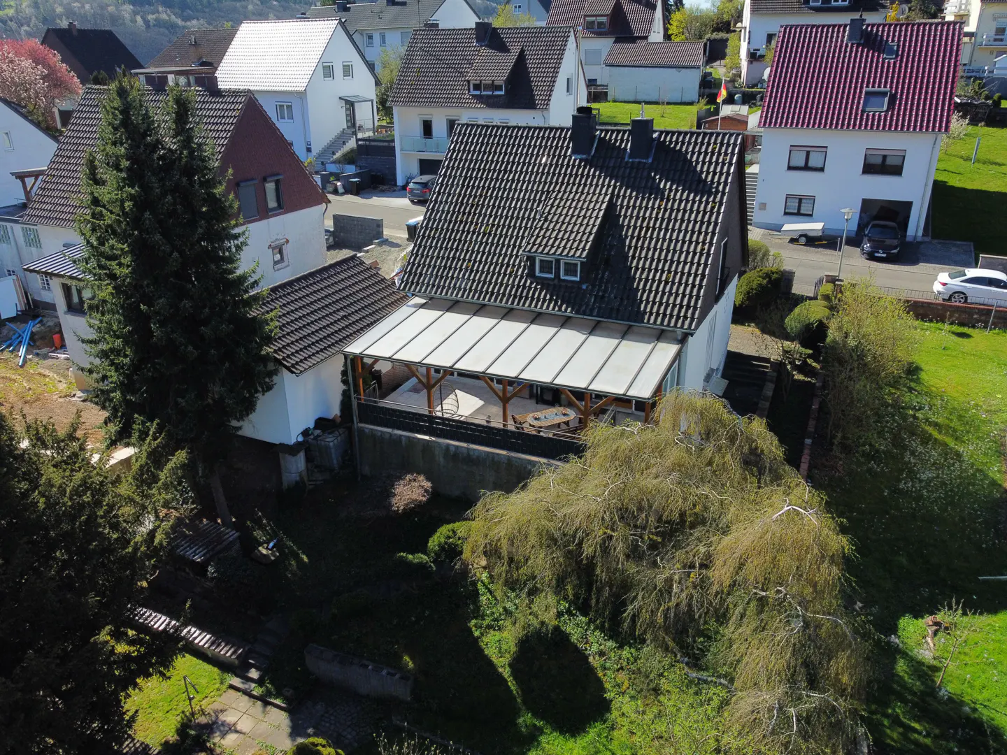 Aerial view of a white house with a gray roof and a covered patio in a residential neighborhood.