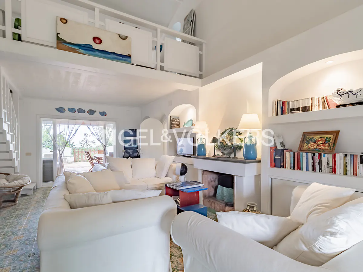 Bright living room with white sofas, a fireplace, and built-in bookshelves. A balcony overlooks the room.