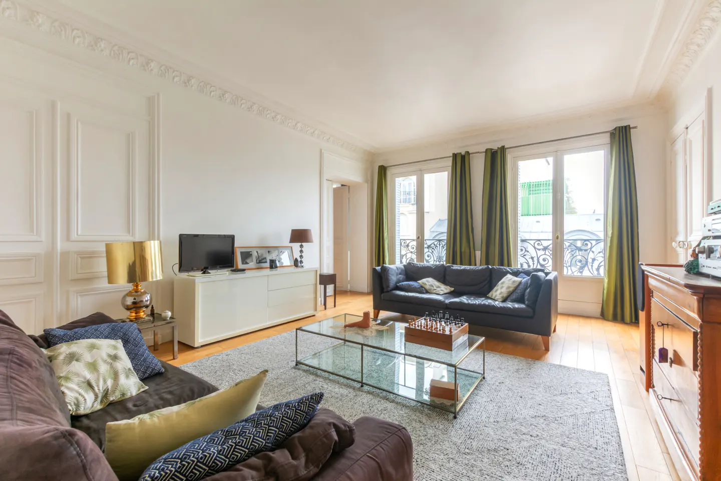 Bright living room with brown and black sofas, glass coffee table with chess set, and white walls with decorative molding.