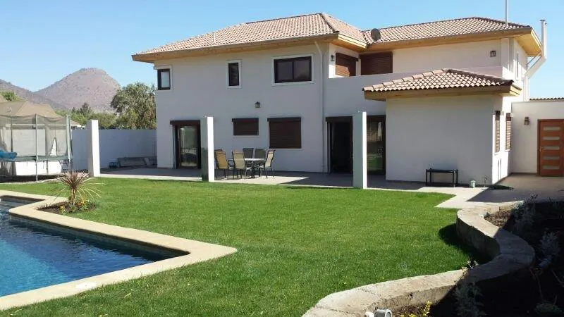 Backyard view of a two-story white house with a brown tile roof, green lawn, and blue pool. A mountain is visible in the background.