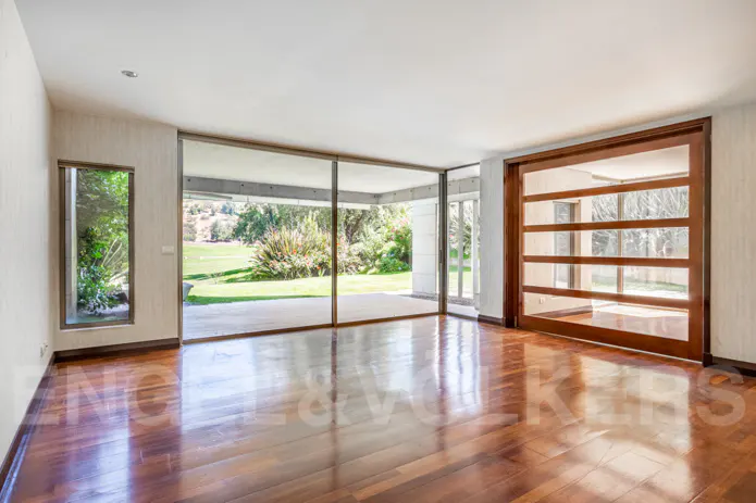 Bright, empty room with hardwood floors, large windows overlooking a green lawn, and a sliding wood-framed glass door.