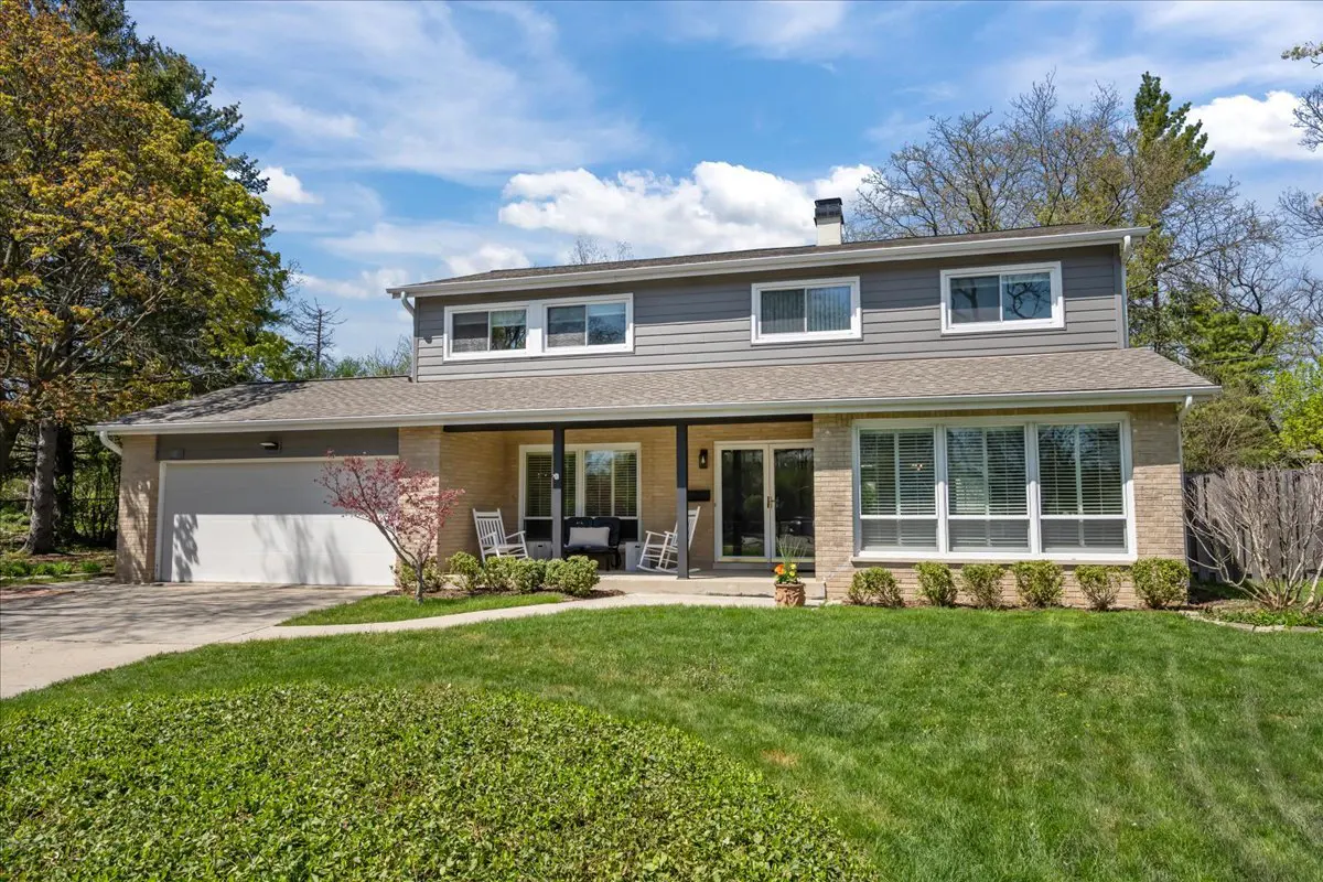 Two-story house with a gray second story, tan brick first story, and a green lawn. Rocking chairs sit on the porch.