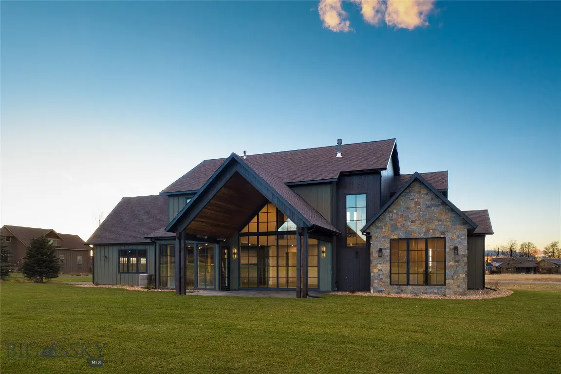 Exterior view of a modern farmhouse with a stone facade, dark trim, and a large covered patio, set against a blue sky.