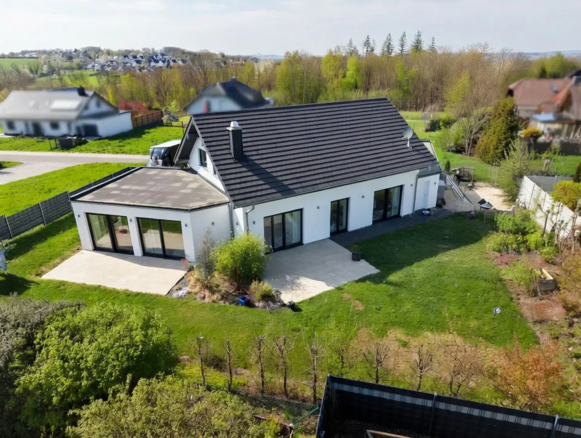 A modern white house with a dark gray roof, surrounded by green lawn and trees.