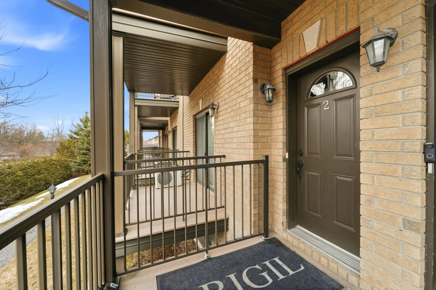 Exterior view of a brick apartment building with a brown door numbered "2" and a black railing.