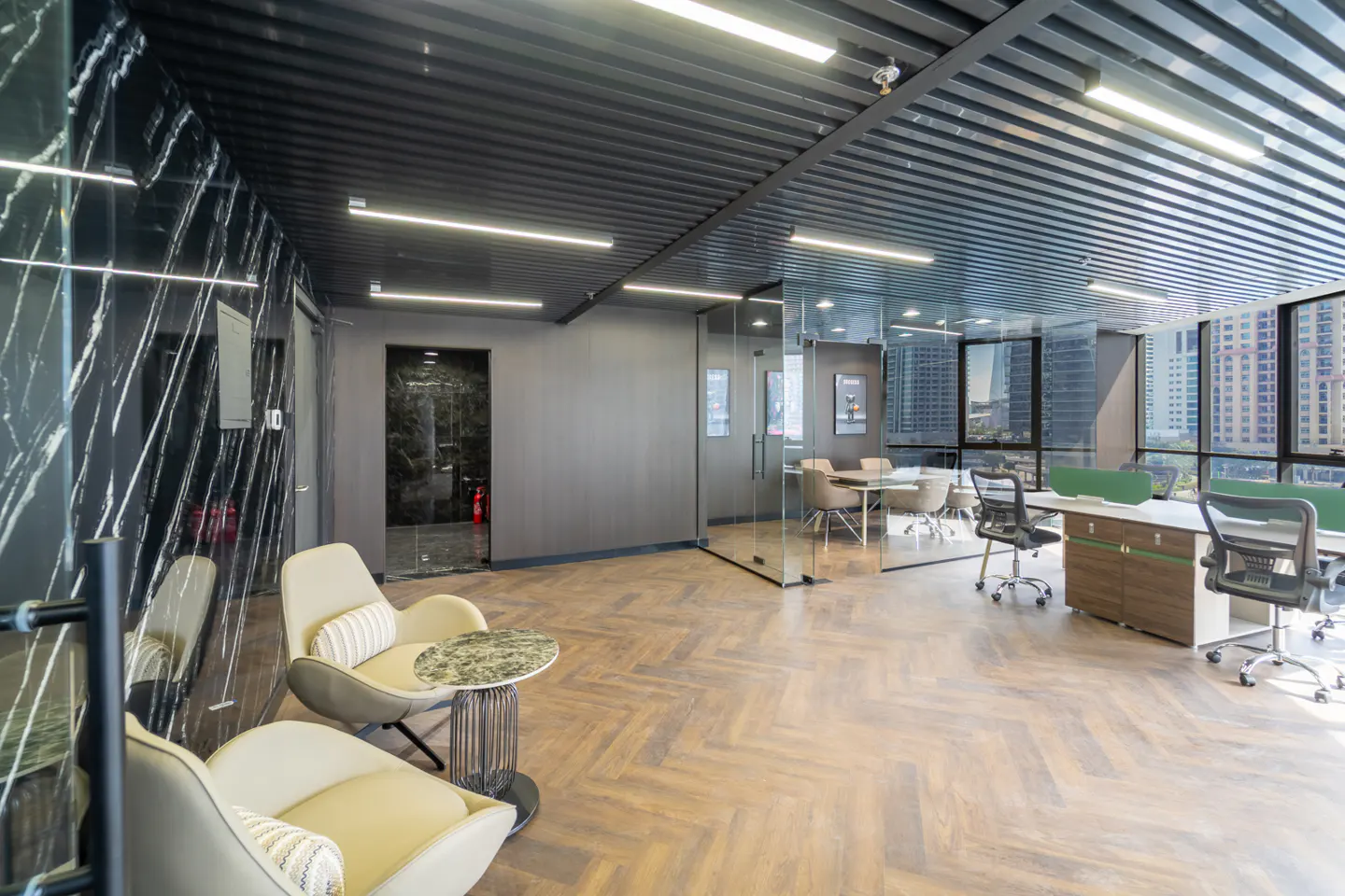 Modern office space with herringbone floors, black marble wall, and glass-enclosed conference room with city views.