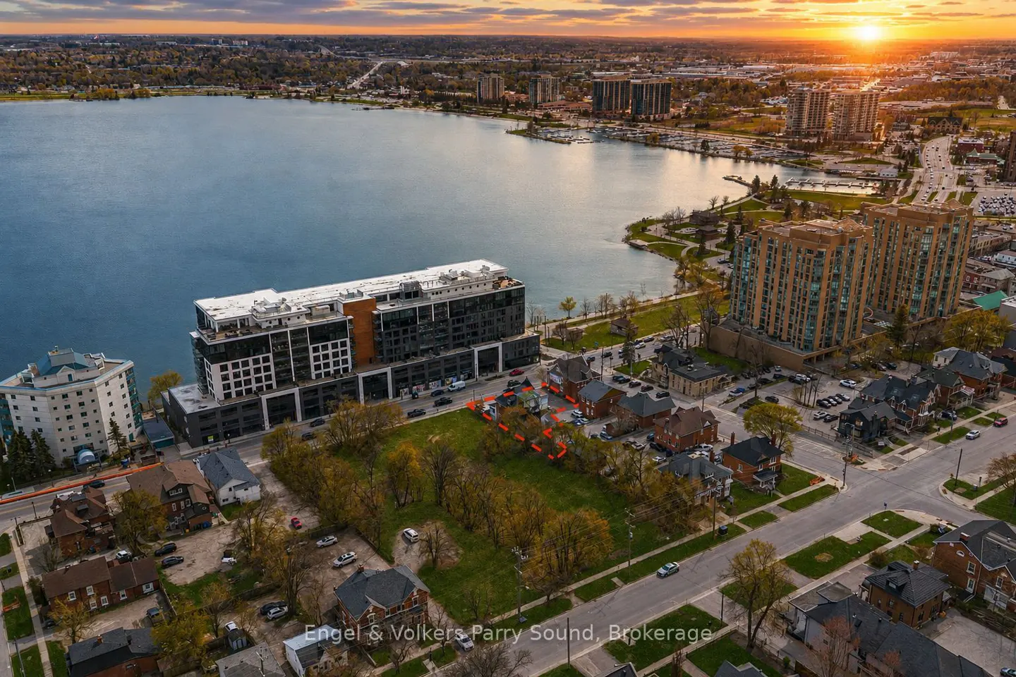 Aerial view of a vacant lot outlined in red, near a lake and buildings at sunset.