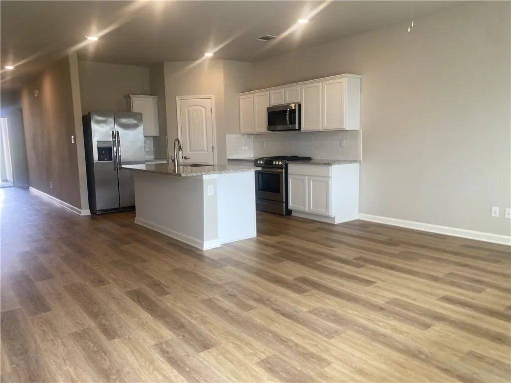 Open-concept kitchen and living area with wood floors, stainless steel appliances, white cabinets, and a kitchen island.