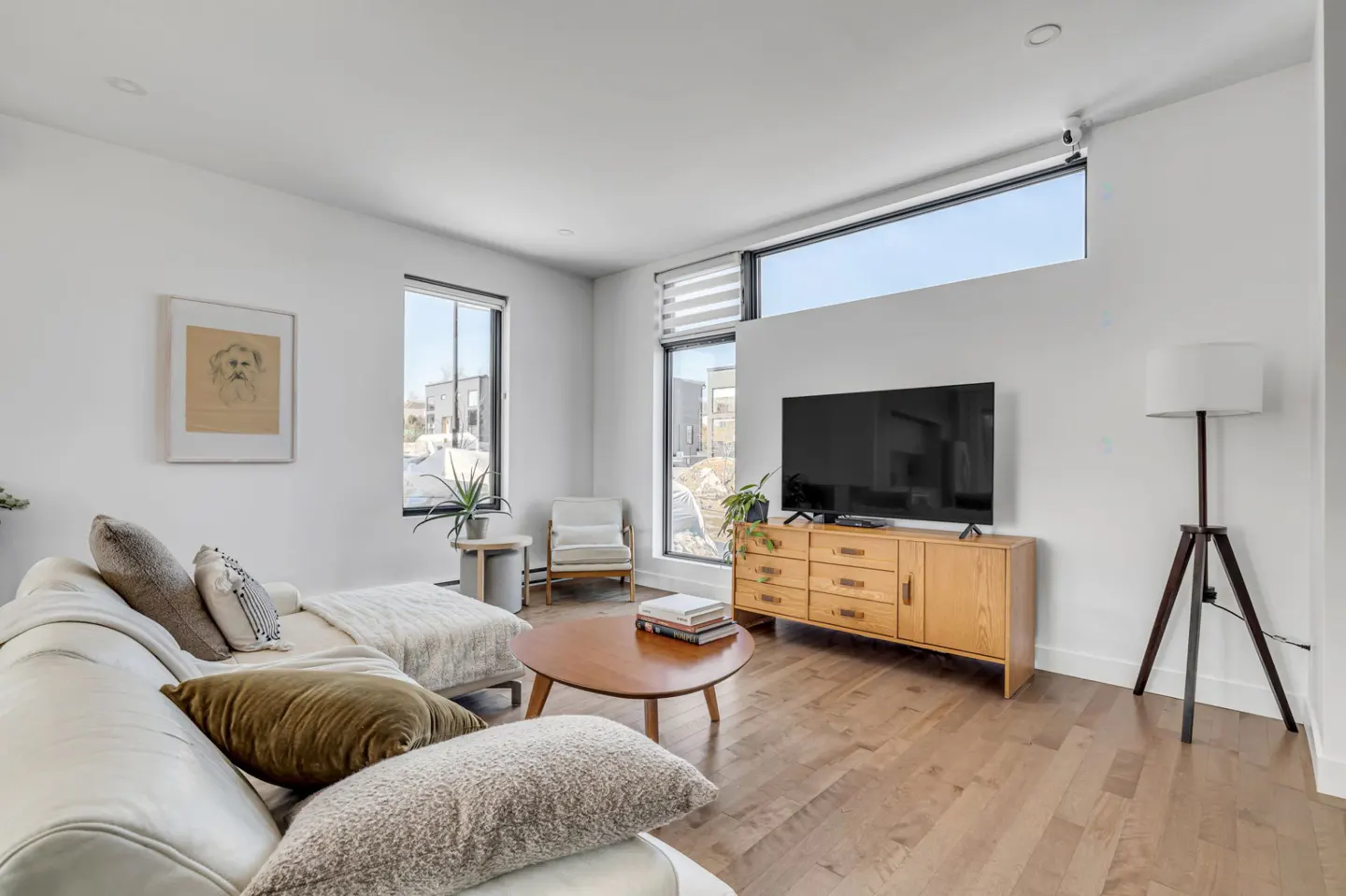 Bright living room with white walls, wood floors, and modern furniture. A large window lets in natural light.