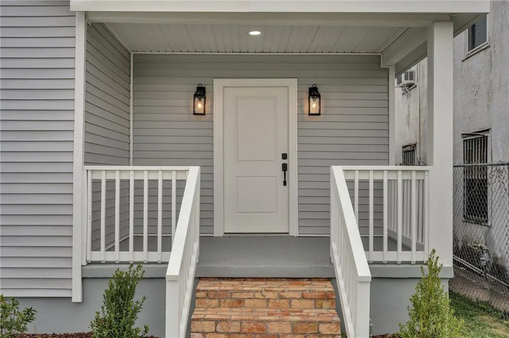 Front porch of a gray house with a white door, white railings, and brick steps. Two black lanterns flank the door.