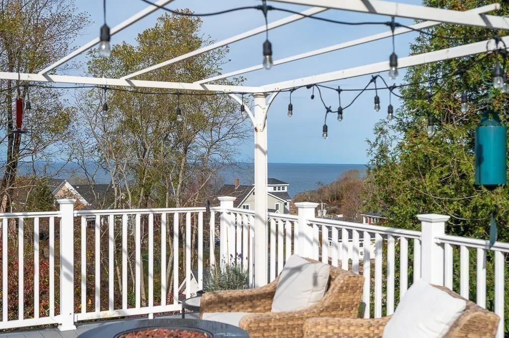 Outdoor patio with wicker chairs, white pergola strung with lights, and a view of the ocean.