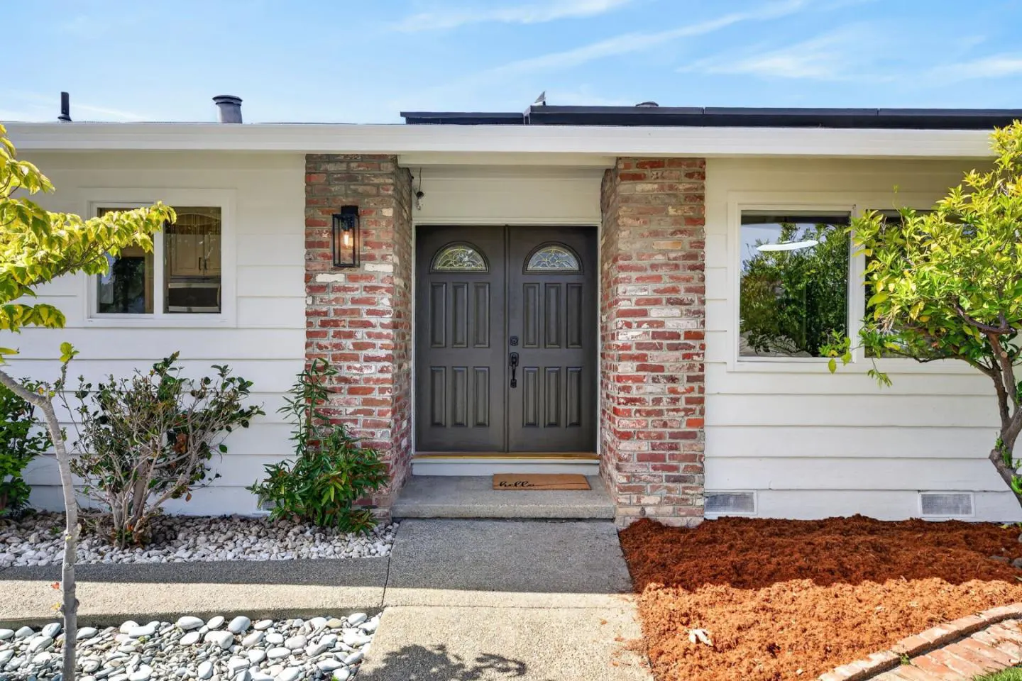 Front entrance of a white house with a brick facade and a dark double door. A walkway leads to the door.