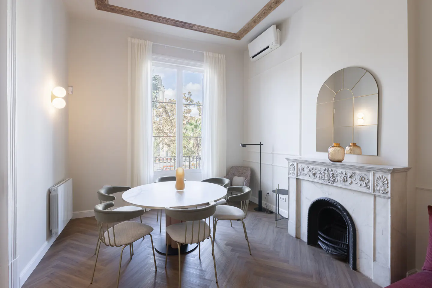 Bright dining room with herringbone floors, a white marble table with six chairs, and a decorative fireplace with a mirror above.
