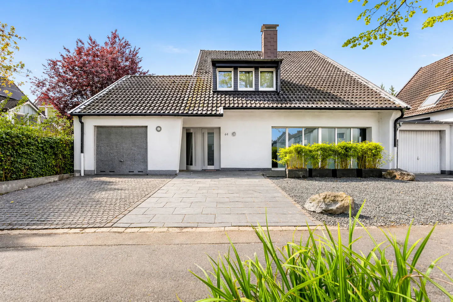 A modern white house with a gray tiled roof, a gray garage door, and a stone walkway.