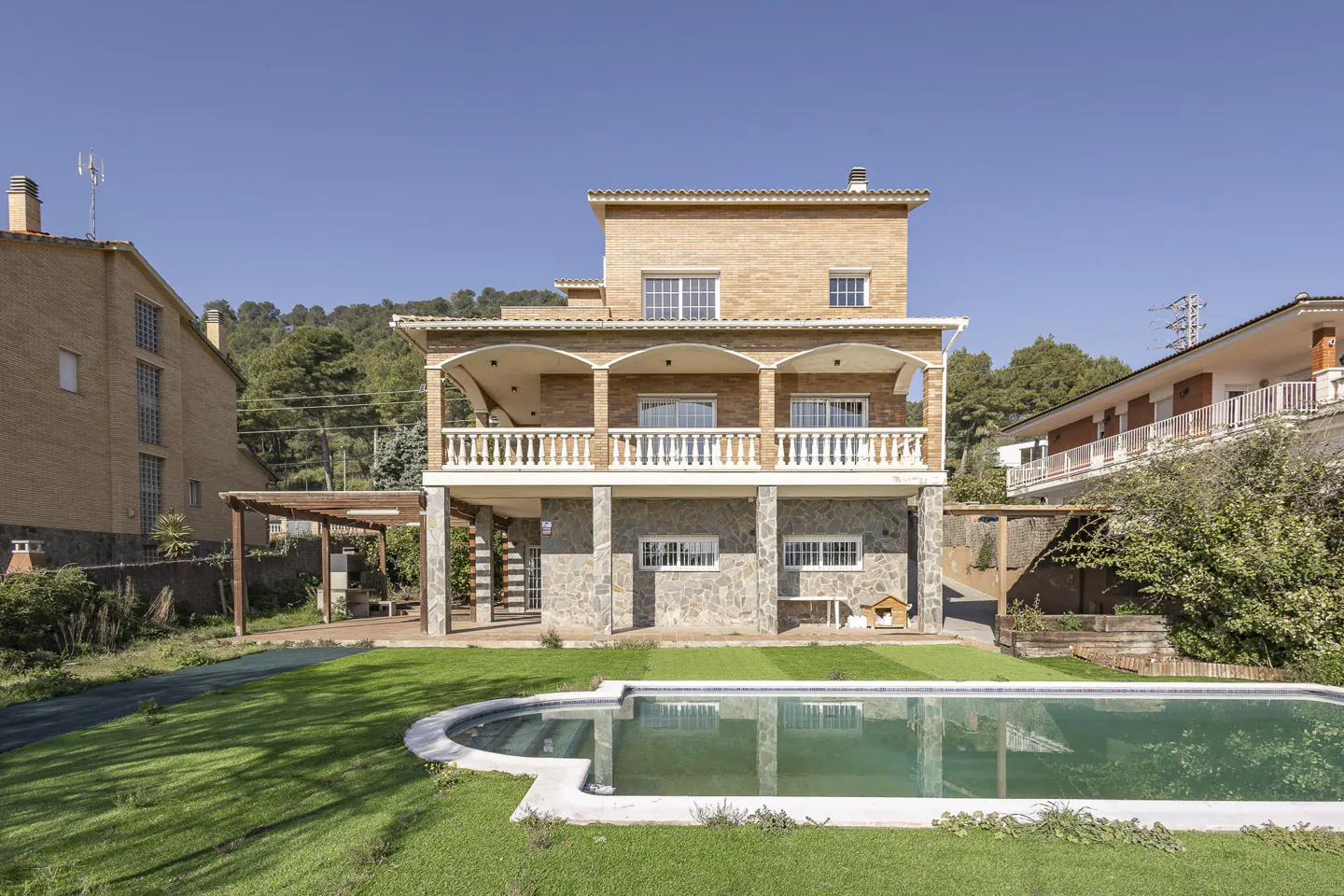 Three-story house with a pool. The house is brick and stone with a white balcony. The pool is surrounded by green grass.