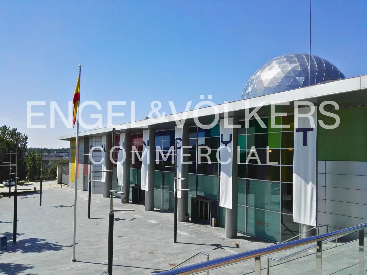 Exterior view of a modern commercial building with colorful panels and a geodesic dome on top, under a clear blue sky.