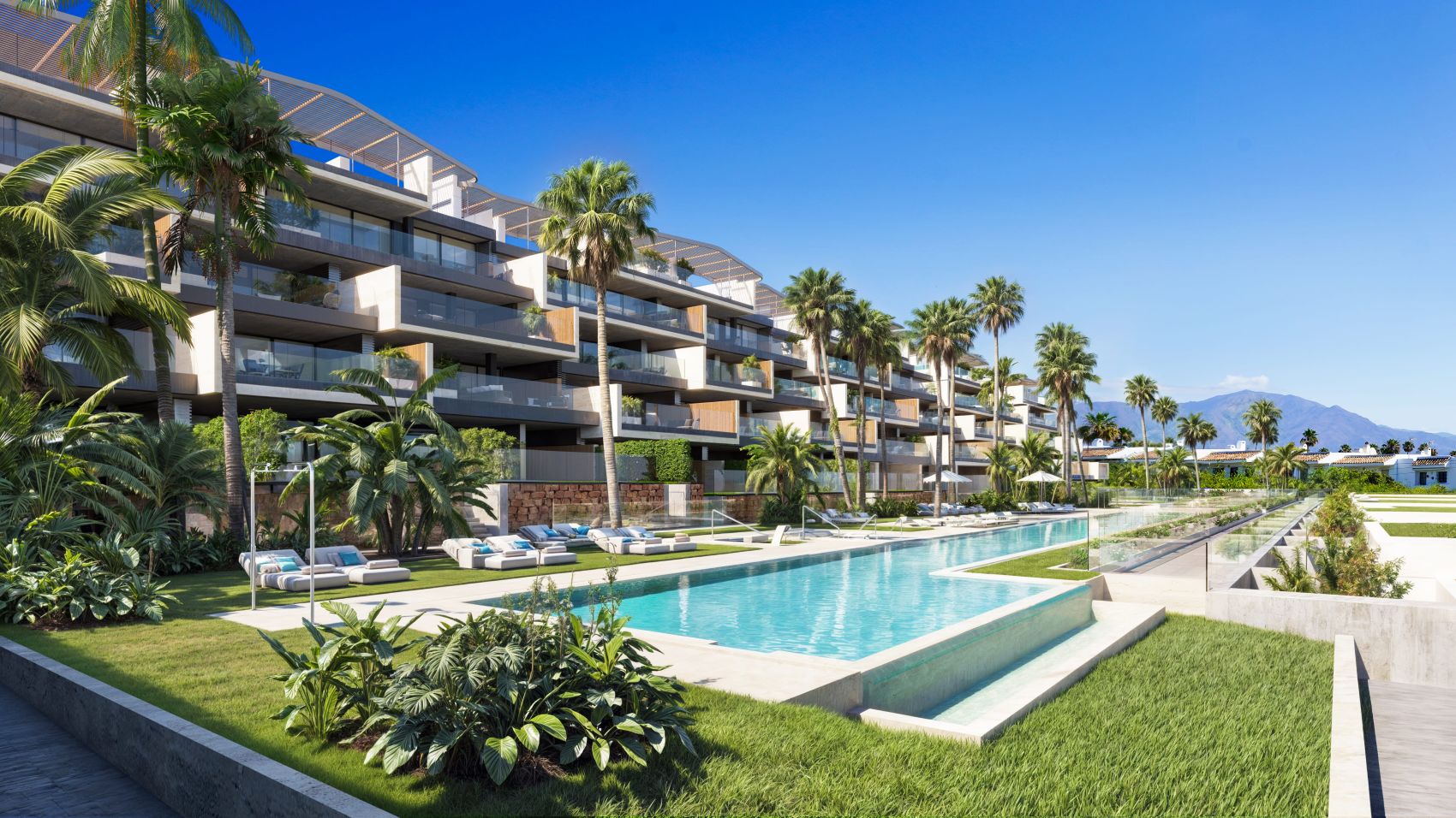 Modern apartment complex with a long swimming pool, palm trees, and lounge chairs on a sunny day with mountain views.