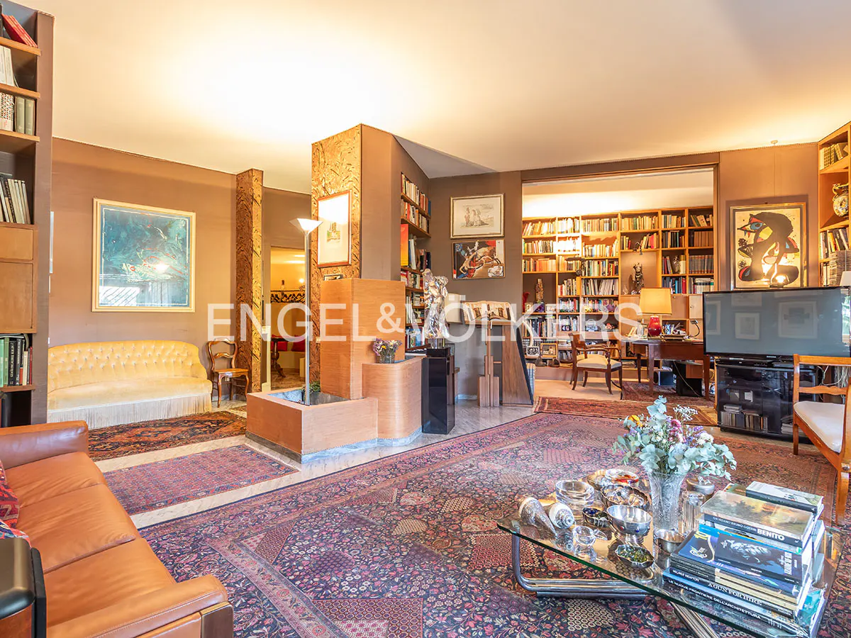 A spacious living room with brown walls, bookshelves, a brown leather sofa, and a glass coffee table.