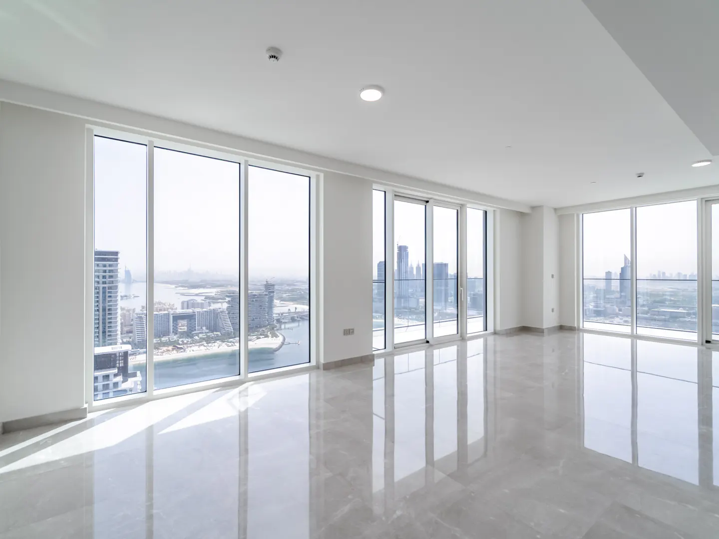 Empty modern apartment with white walls, glossy marble floors, and floor-to-ceiling windows overlooking a city skyline.