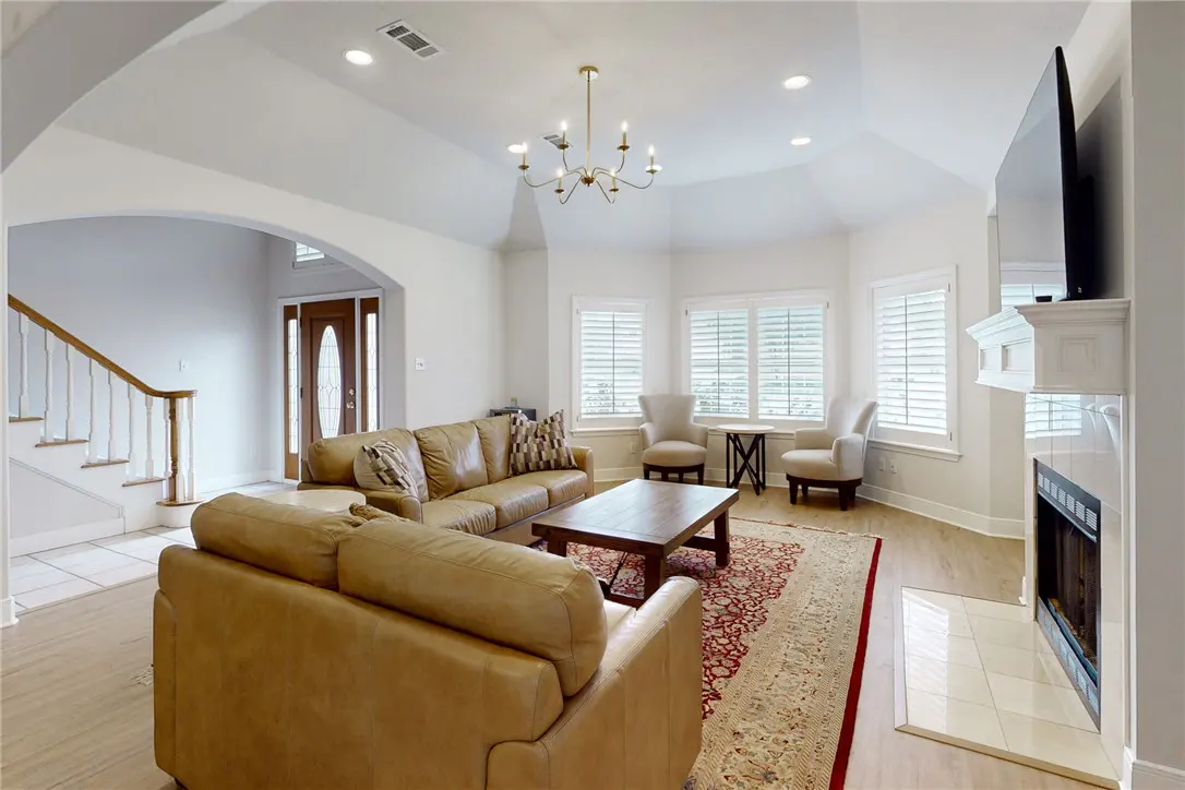 Bright living room with tan leather sofas, wood coffee table, fireplace, and red patterned rug. Windows with white shutters.