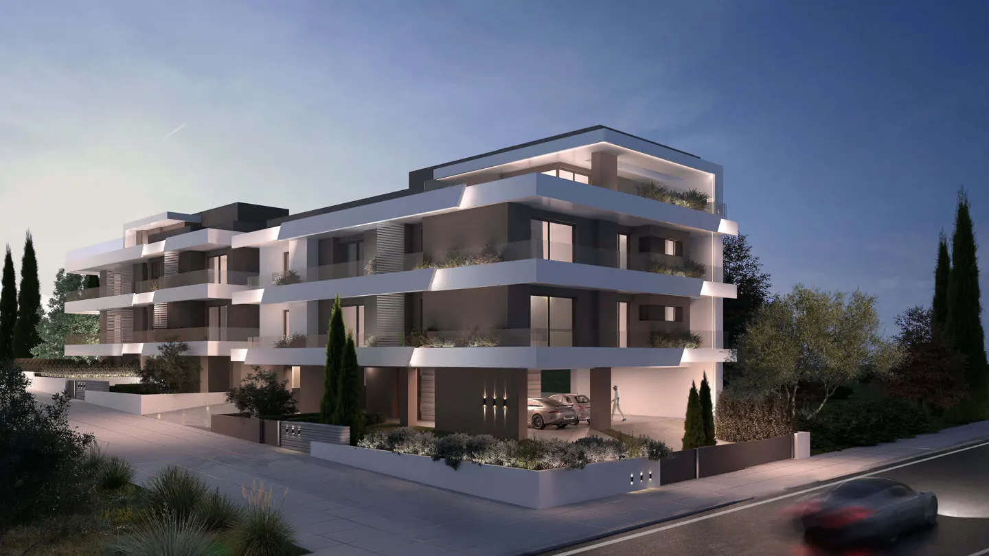 Modern gray and white apartment building with balconies at dusk. A car drives by on the wet street.