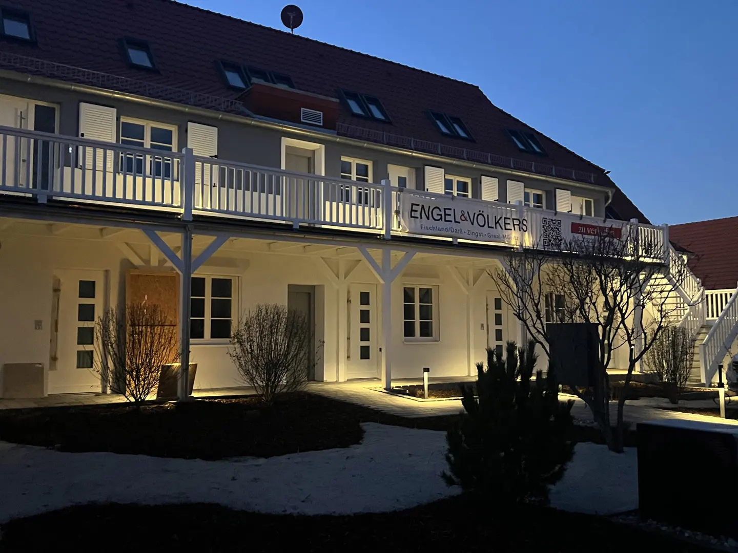 Exterior of a two-story building with white trim and an Engel & Völkers banner at dusk.