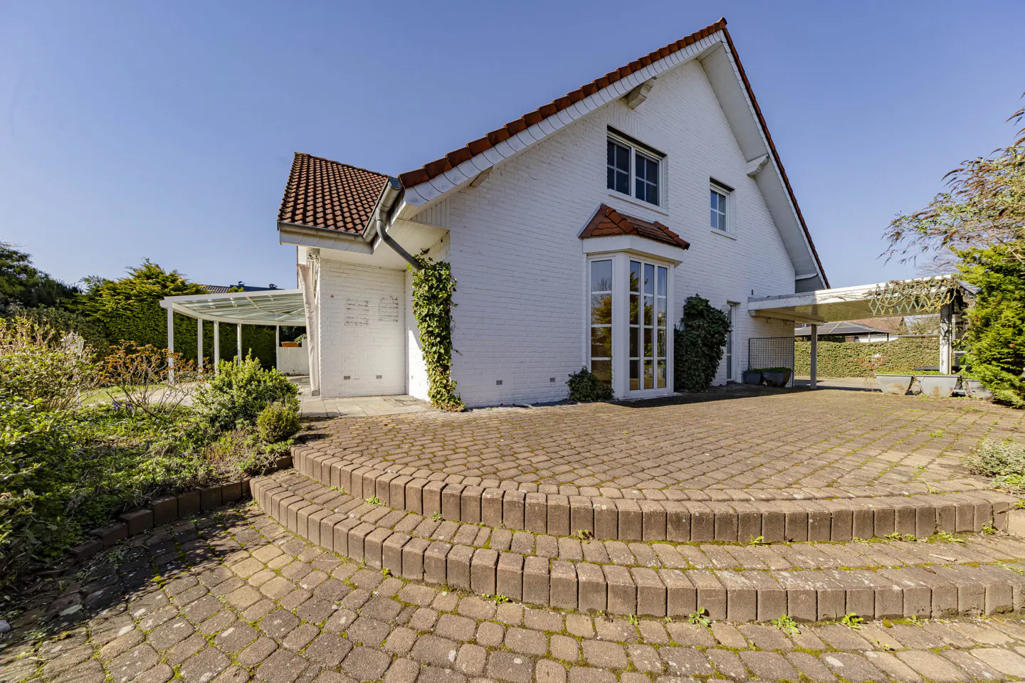 Exterior view of a white brick house with a red tile roof and a brick patio.