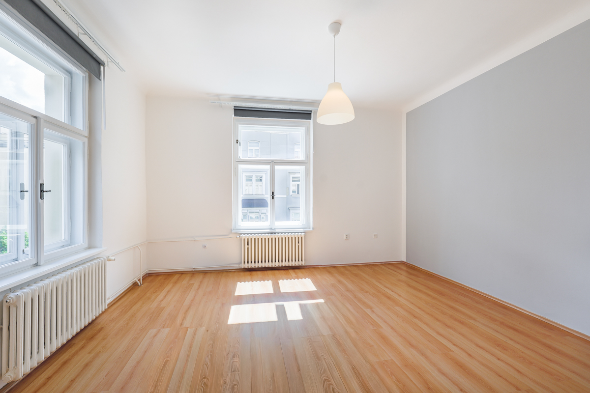Empty room with light wood floors, white walls, a grey accent wall, two windows with radiators, and a pendant light.