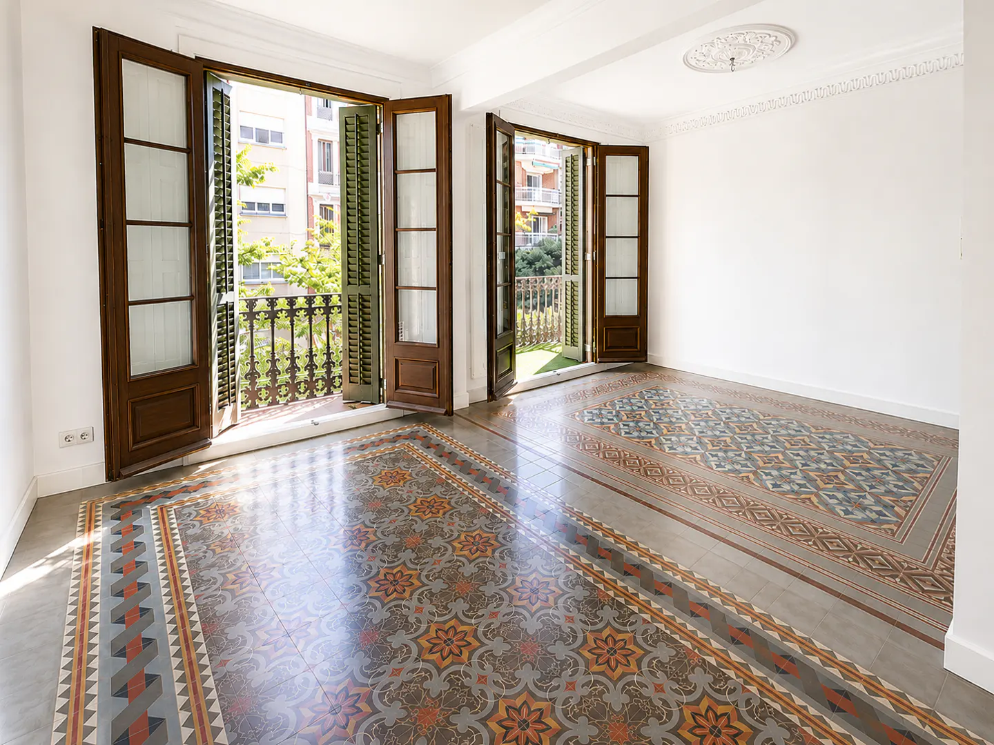 Bright, empty room with ornate patterned tile floors, white walls, and two sets of open wooden doors leading to balconies.
