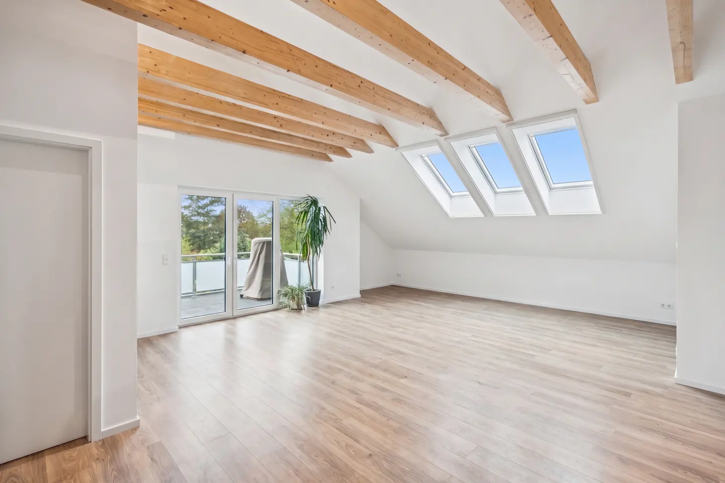 Bright, empty attic room with wood floors, white walls, exposed beams, skylights, and a balcony.