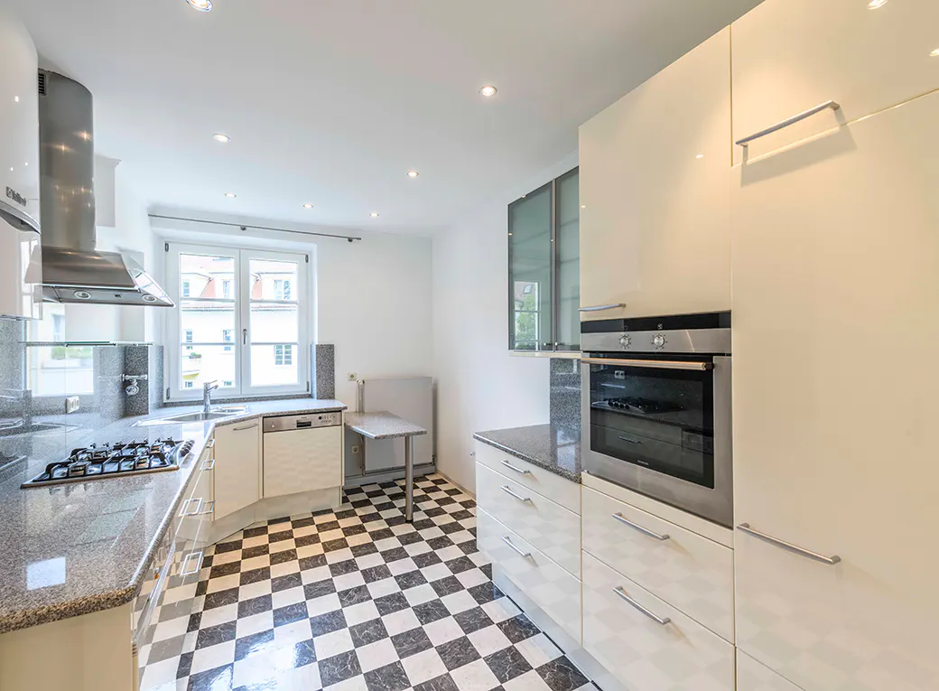 Bright kitchen with black and white checkered floor, white cabinets, granite countertops, stainless steel appliances, and a window.