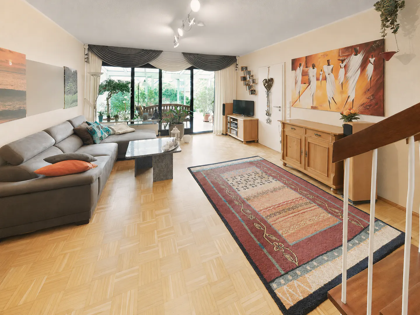 Spacious living room with a grey sectional sofa, patterned area rug, wooden sideboard, and large windows overlooking a patio.