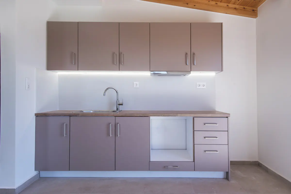 Modern kitchen with mauve cabinets, wood countertop, stainless steel sink, and under-cabinet lighting against white walls.
