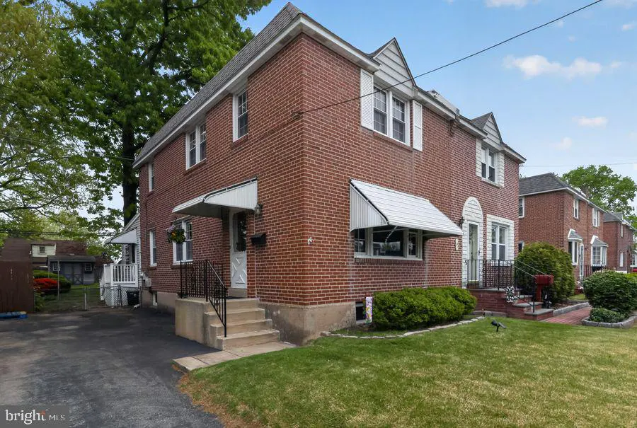 Red brick row house with white trim, awnings, and a small front lawn on a sunny day.