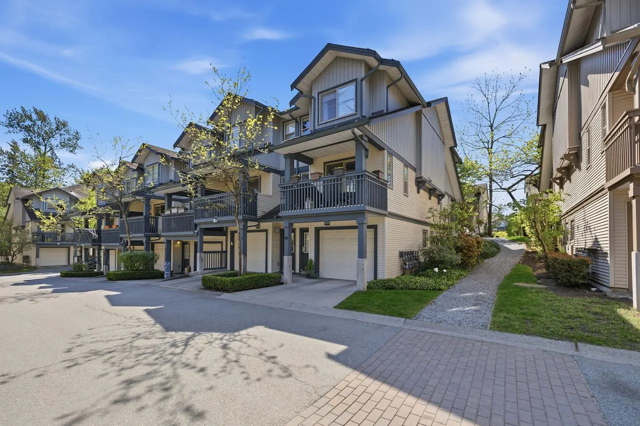 Exterior view of multi-story townhouses with balconies and garages on a sunny day.