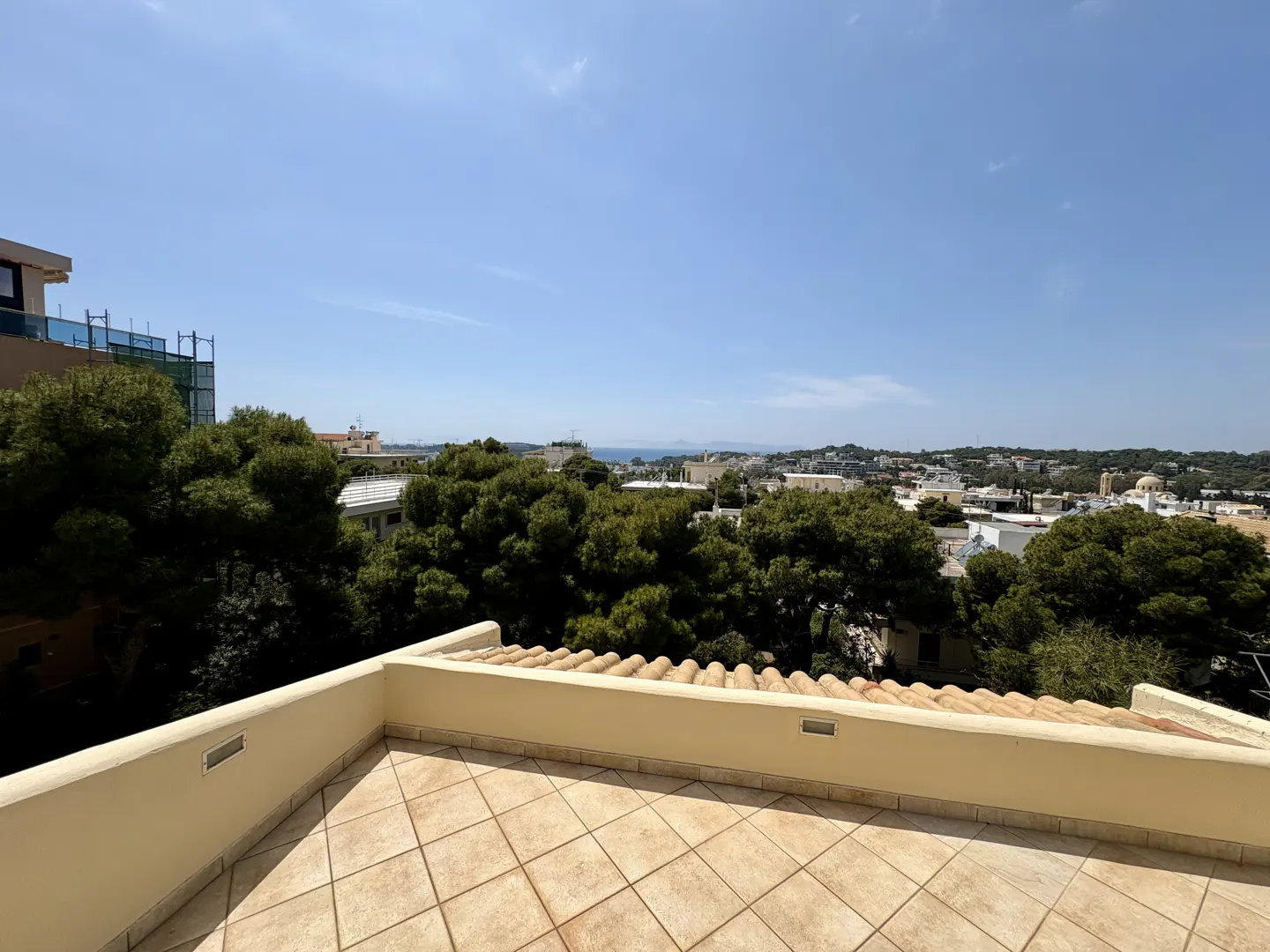 View from a tiled balcony overlooking green trees and a townscape under a clear blue sky.