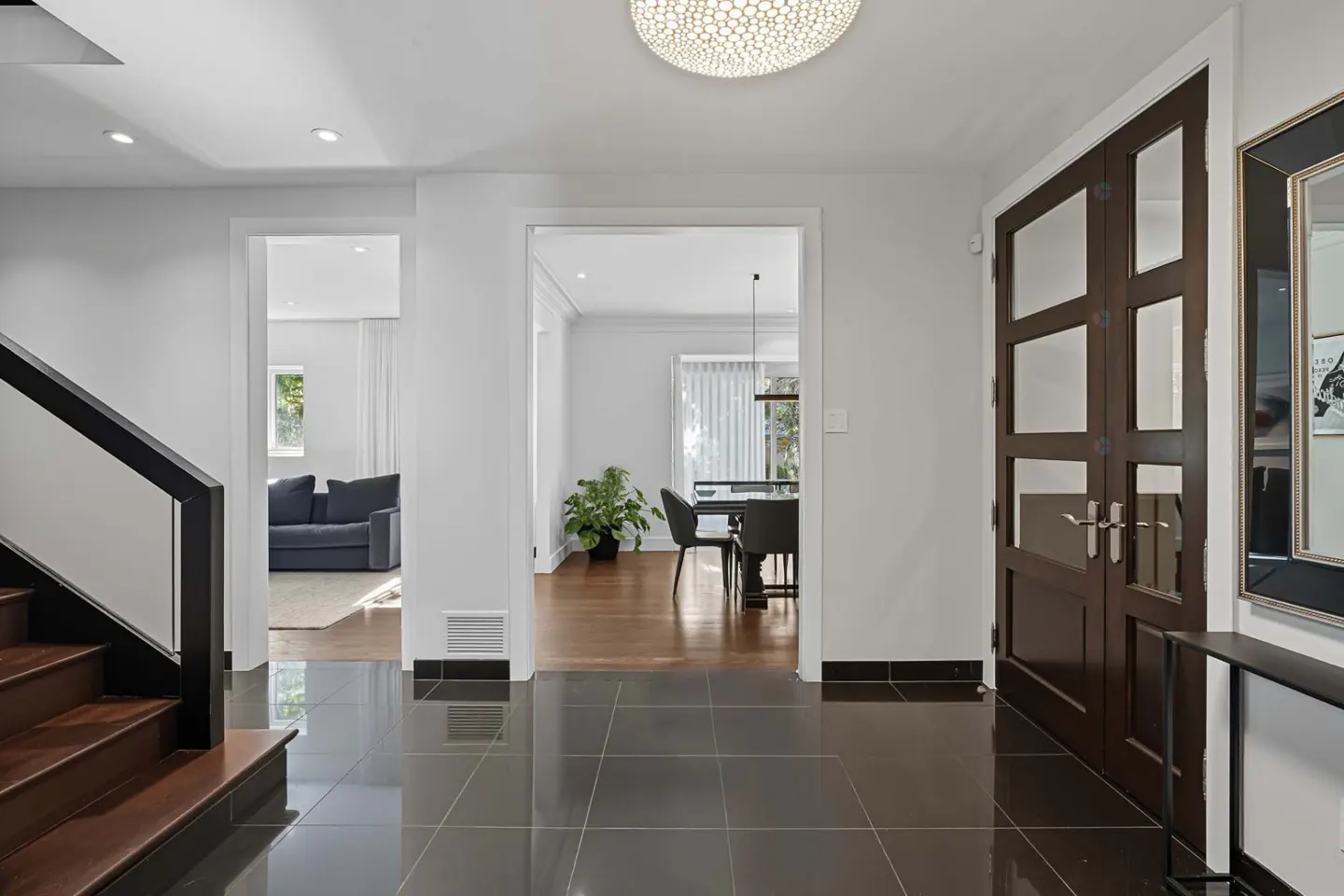 Entryway with dark tile floor, white walls, and dark wood doors. A staircase is on the left and a dining room is visible through an archway.